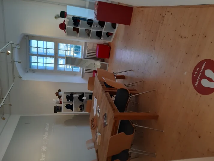 Blick in die Ausstellung Kopfsache im Brotmuseum: Im Hintergrund zwei Regal mit Hüten zum Aufprobieren, davor ein großer Tisch mit Bastel- und Schreibmaterial