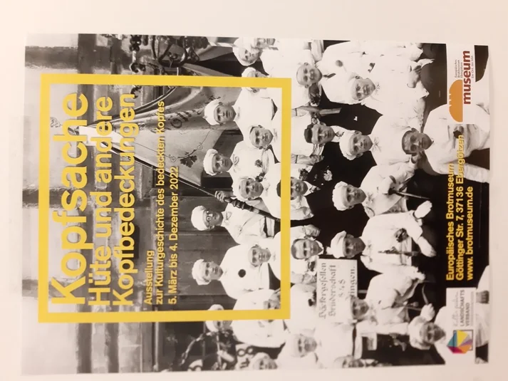 Flyer der Ausstellung Kopfsache: Ca 100 Jahre altes Schwarz-weiß Bild von Bäckergesellen mit Bäckermütze, darüber in einem gelben Kasten der Titel der Ausstellung