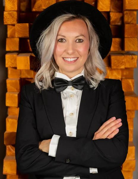 Eine blonde Sängerin im schwarzen Anzug mit Fliege und Hut lächelt in die Kamera