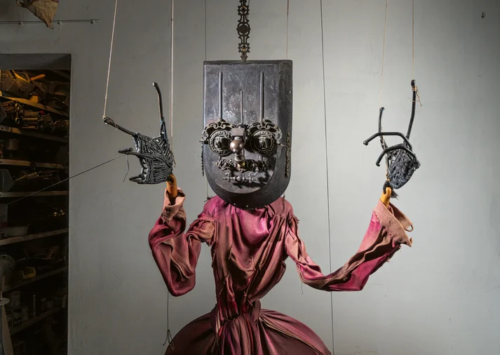 Eine Marionette mit rotem Kleid, langen Fingern und einem großen Gesicht.