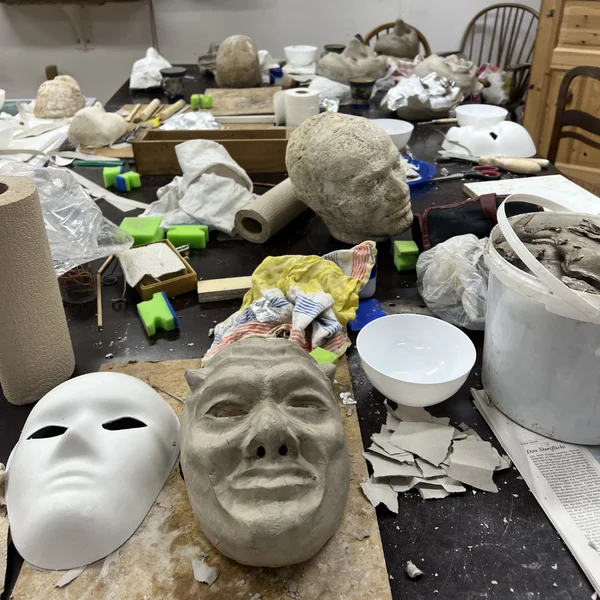 Mehrere Masken liegen in unterschiedlichen Baustufen auf der Werkbank