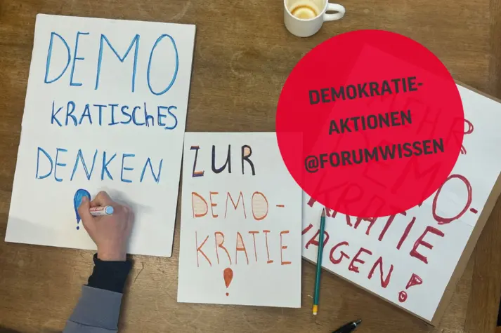 Eine Kinderhand malt an einem Demoplakat auf einem Tisch.