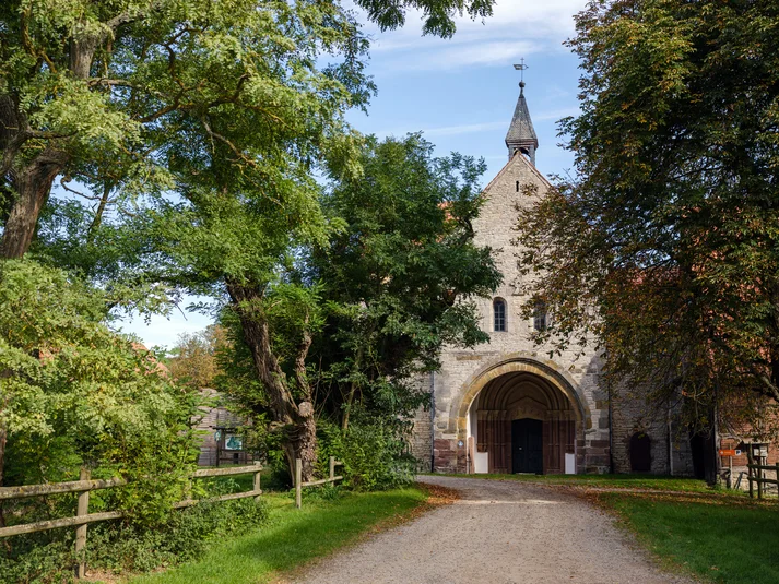 Eingang zur Klosterkirche Wiebrechtshausen. Links und rechts ragen grüne Bäume in das Bild.