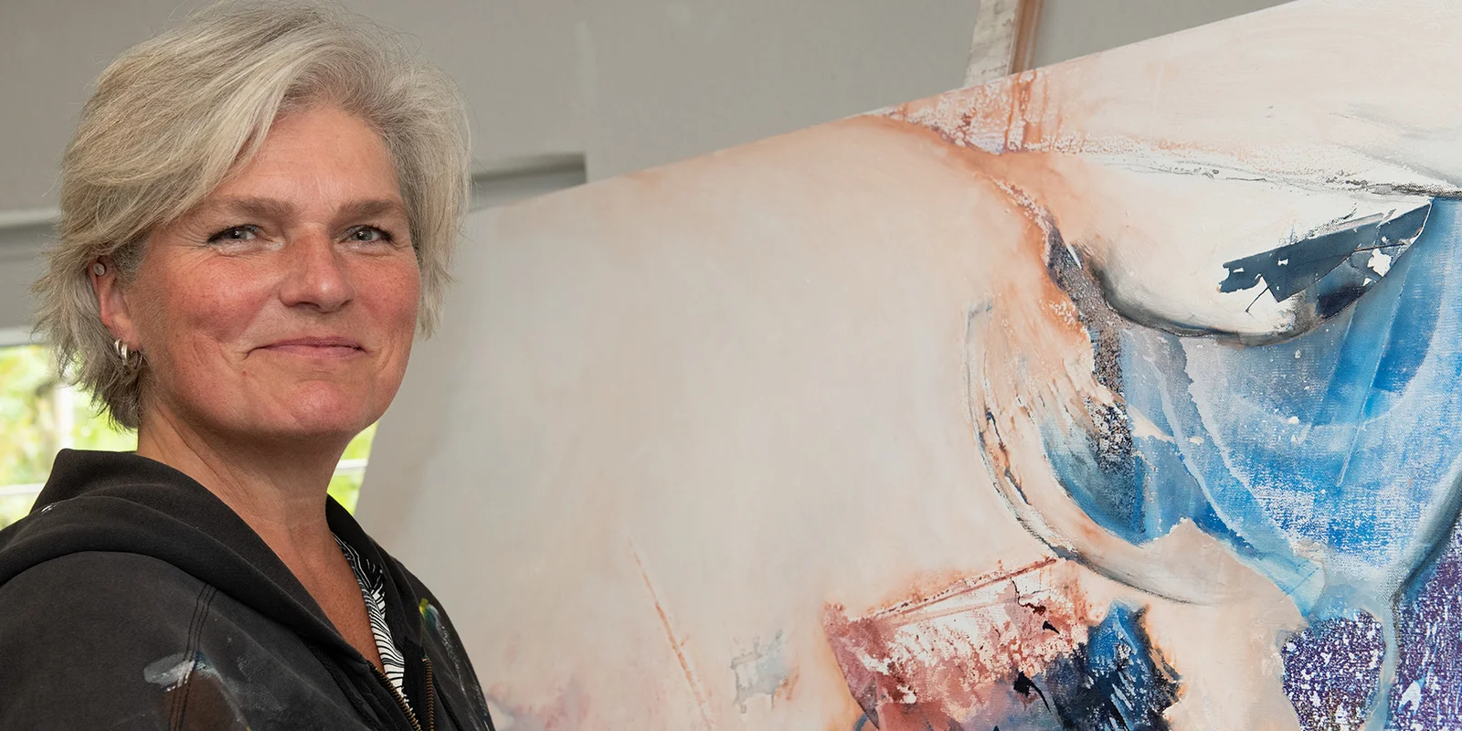 Hiltrud Esther Menz steht lächelnd vor einem abstrackten Bild.