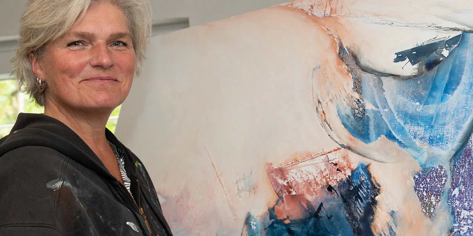 Hiltrud Esther Menz steht lächelnd vor einem abstrackten Bild.