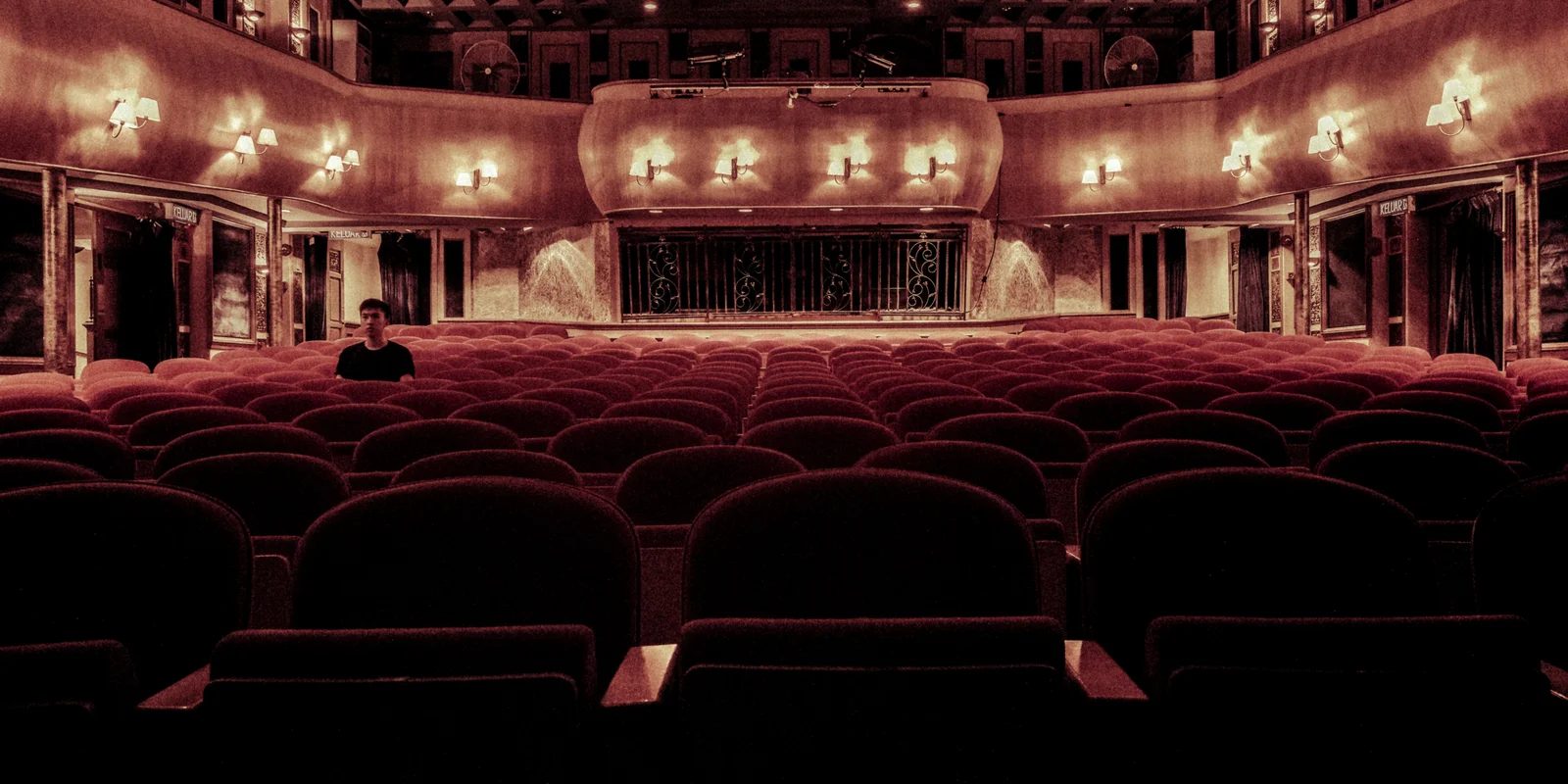 Ein Mann sitzt einsam im Zuschauerraum eines großen Theatersaals.