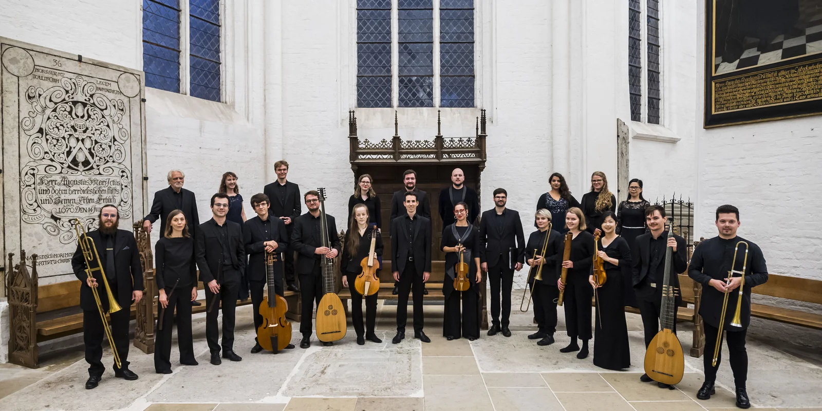 Eine Gruppe Musiker:innen steht schwarz gekleidet in einer weißen Kirche