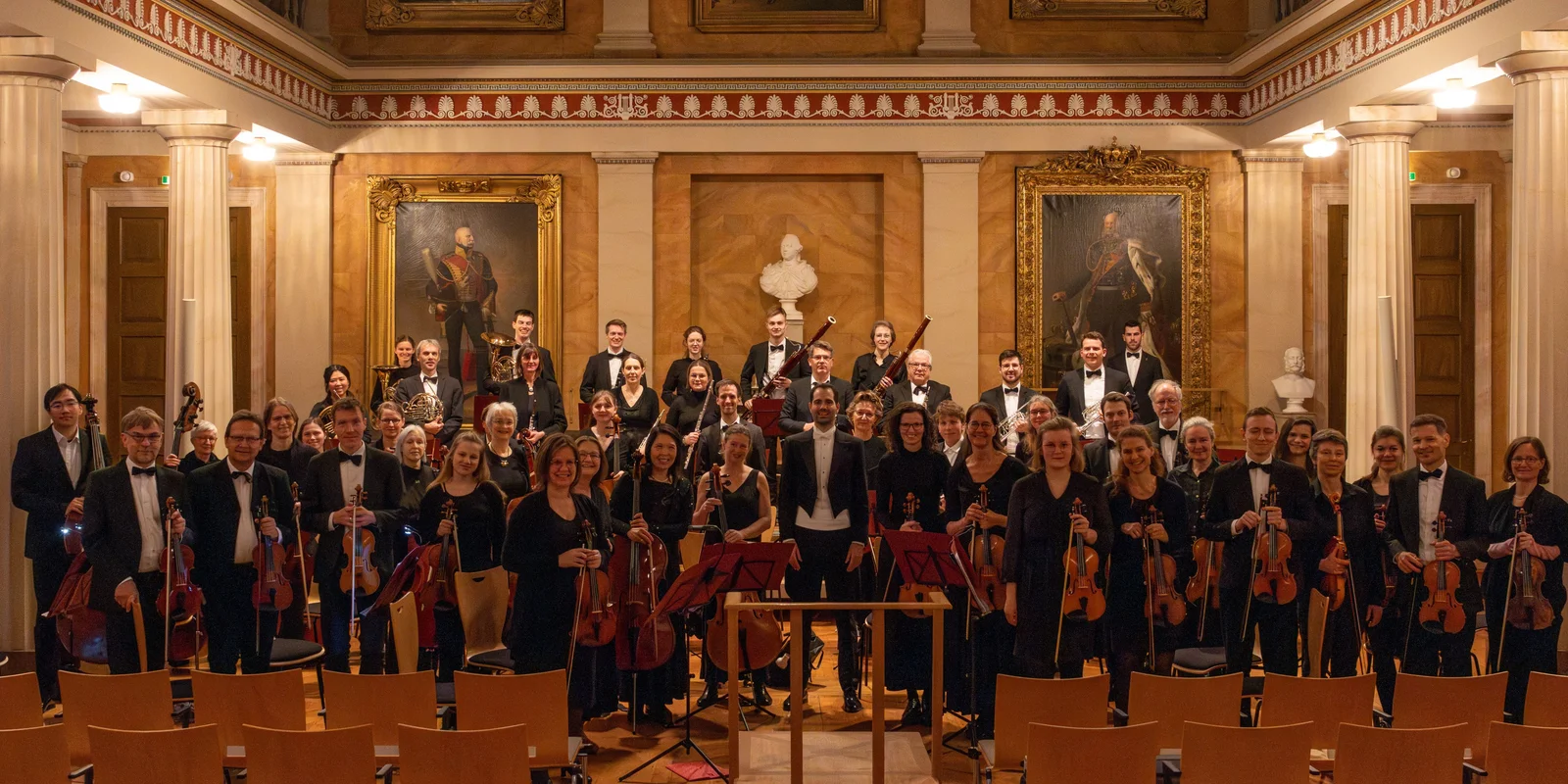 Orchester stehend in schwarz gekleidet mit Instrumenten