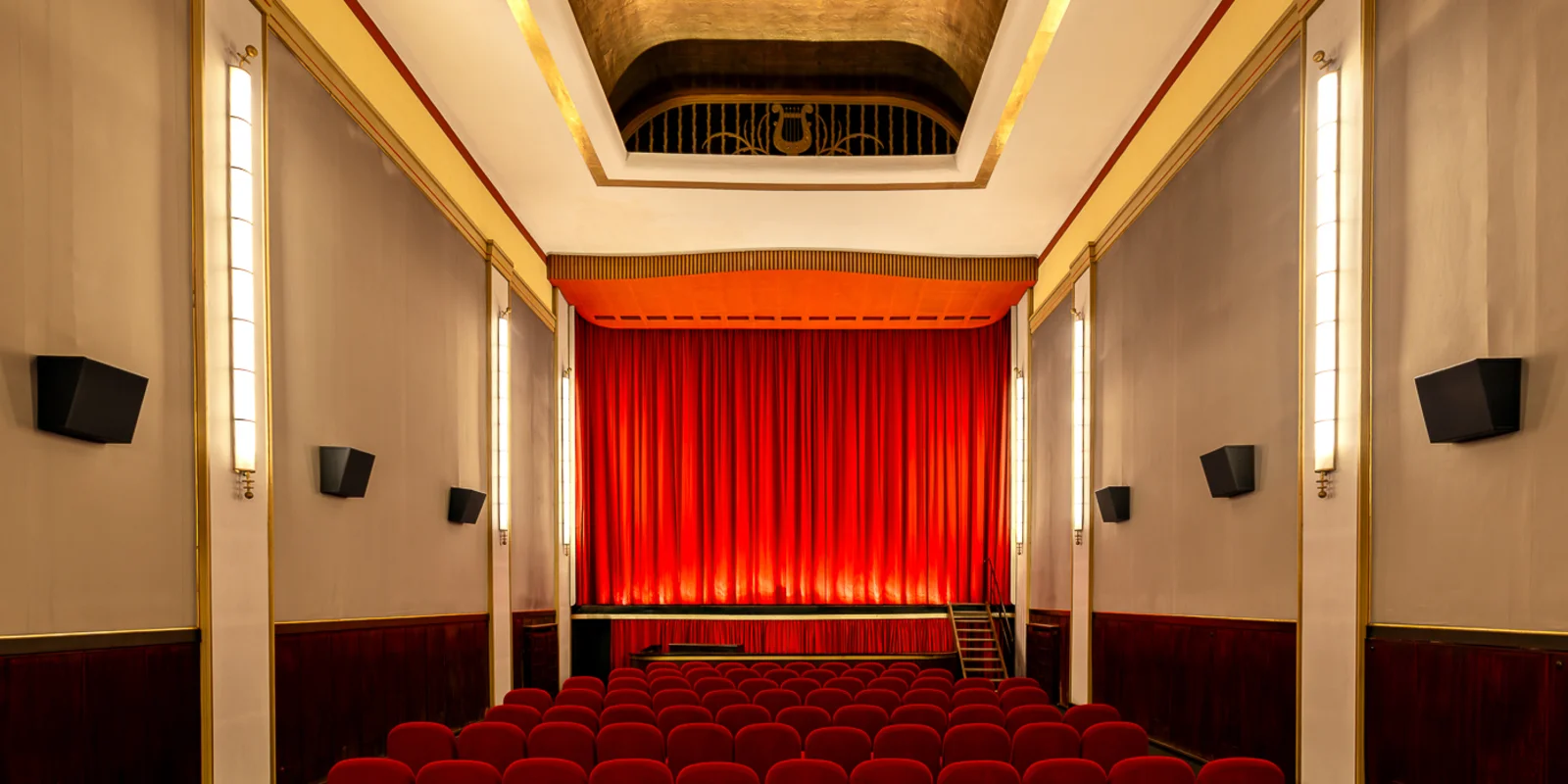 Blick über die roten Kinosessel auf den erleuchteten roten Vorhang des Kinosaals