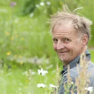 Nik J. Lucht lächelt in die Kamera, er ist umgeben von grünen Pflanzen.