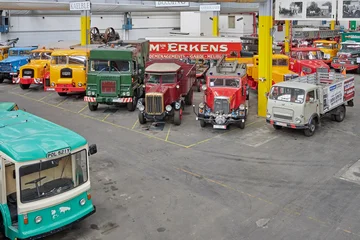 Mehrere Oldtimer-Busse und -LKW stehen in einer großen Depot-Halle.