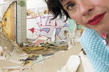 Sonja Elena Schroeder ist unscharf in der oberen rechten Ecke des Bildes zu sehen. Im Hintergrund ist das Innere eines zerstörten und mit Graffitti bemahlten Gebäudes zu sehen.