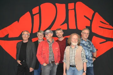 Die sechs Mitglieder der Band Midlife Crises stehen vor einer schwarzen Wand. Auf dieser ist in roter Farbe Midlife Crises in Form eines Mundes geschrieben.