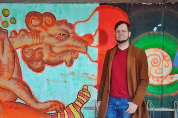 Florian Schäfer steht lächelnd vor einer Wand mit Graffiti-Kunst.