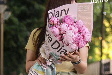 Frau hält Blumenstrauß, der in Zeitungspapier eingewickelt ist
