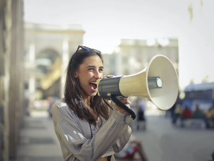 Eine Frau steht auf der Straße und ruft etwas in ein Megafon
