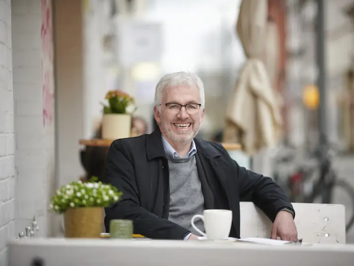 Der Leiter der Händel Festspiele Jochen Schafsmeier sitzt an einem Tisch und lächelt in die Kamera