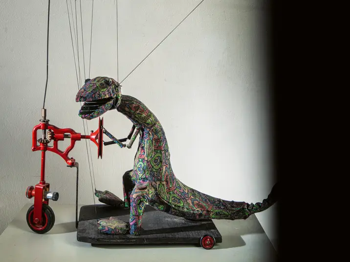 Eine Dinosauriermarionette auf einem Tretroller
