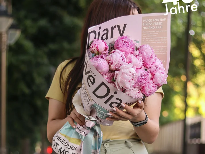 Frau hält Blumenstrauß, der in Zeitungspapier eingewickelt ist