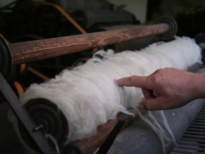 Eine Finger zeigt auf die weißen Fäden einer historischen Spinnereimaschiene