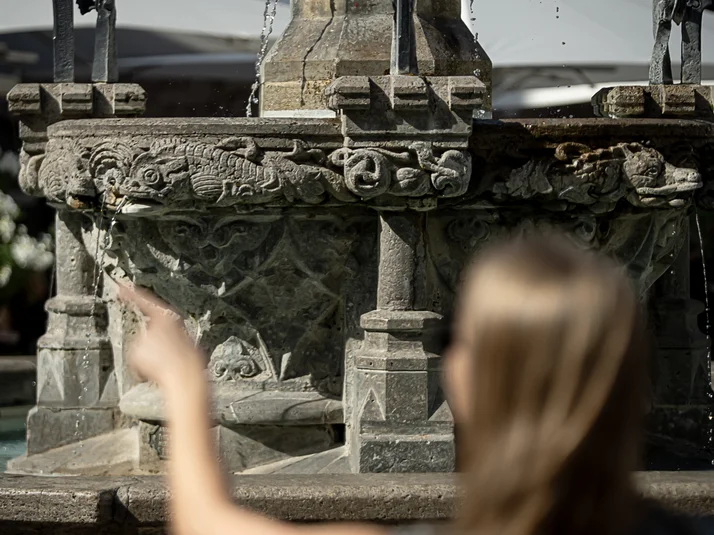 Im Vordergrund (unscharf) junge Frau zeigt auf Gänselieselbrunnen